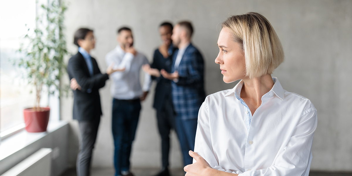 Male Coworkers Whispering Behind Back Of Unhappy Businesswoman Spreading Rumors And Gossips Standing In Modern Office. Sexism And Bullying Problem At Workplace Concept. Selective Focus